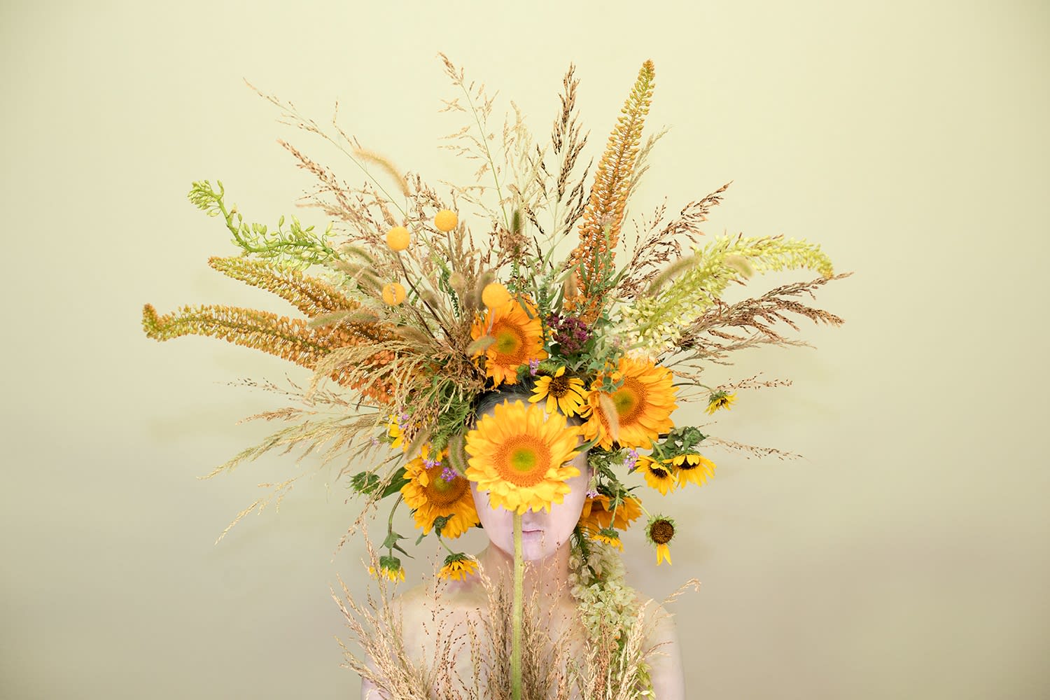 Photograph of girl surround in flowers and sunflowers, covering her face