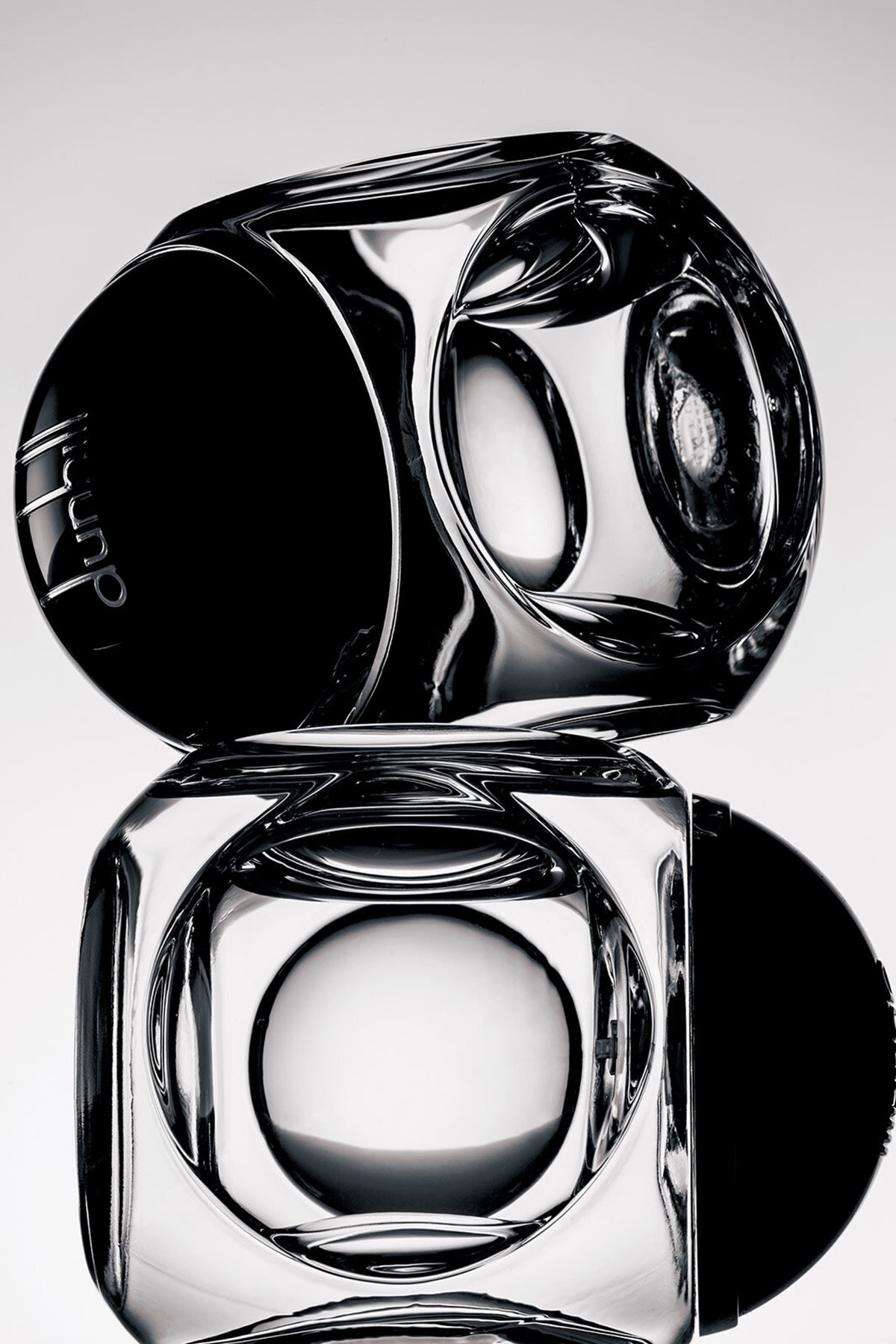 Two Dunhill Century fragrance bottles, both on their sides, balanced on top of each other, in black and white. 