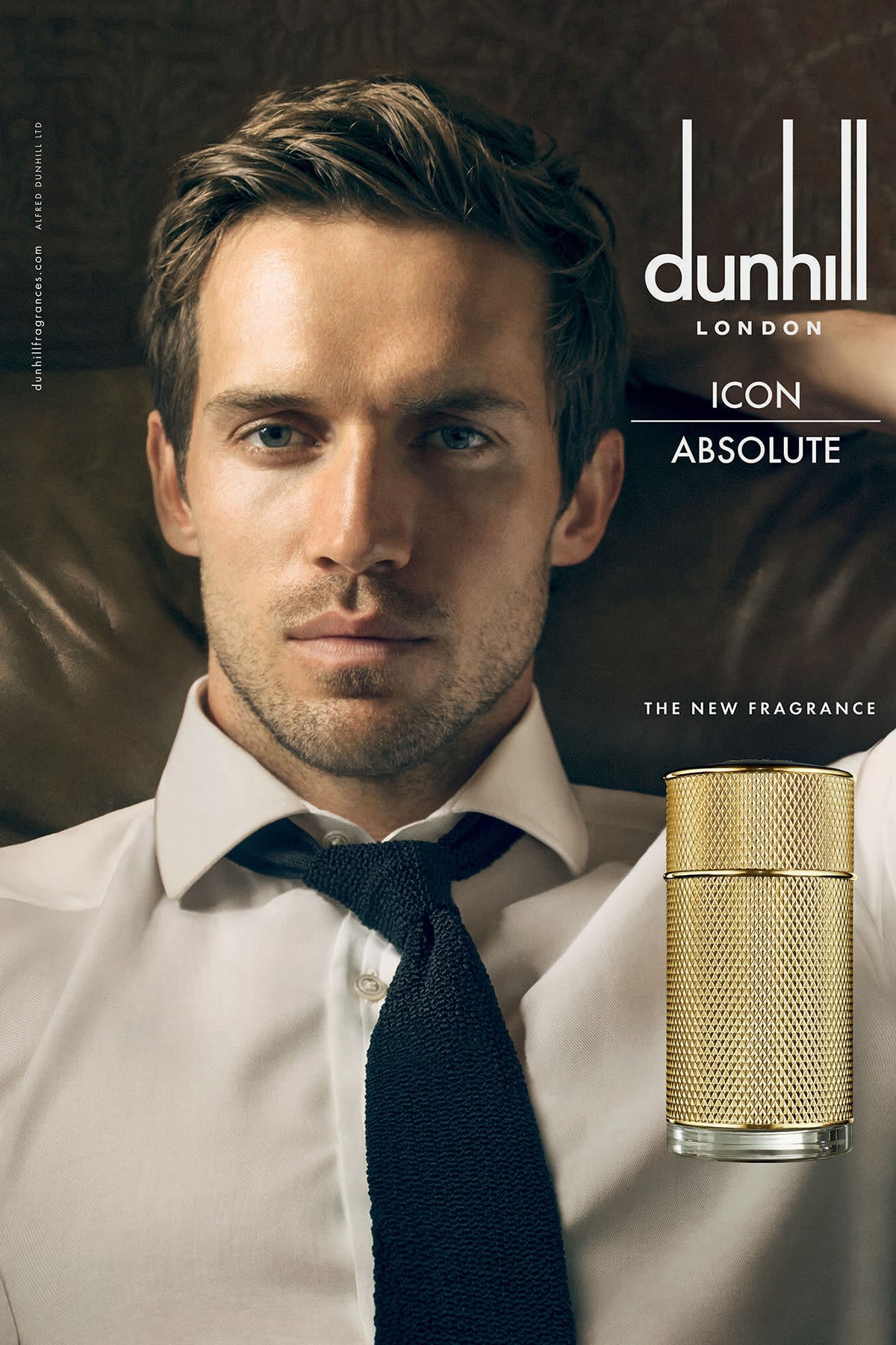 An Advert depicting a front on view of man wearing an unbuttoned white shirt with a loose tie. In the bottom right hand corner is a front view of a gold Dunhill Icon Absolute fragrance bottle. 