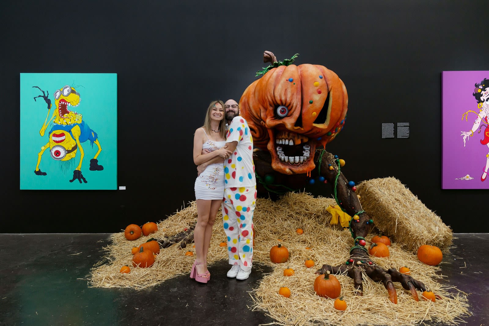 Alex Pardee and Chloe Rice hugging in front of Giant Pumpkin installation