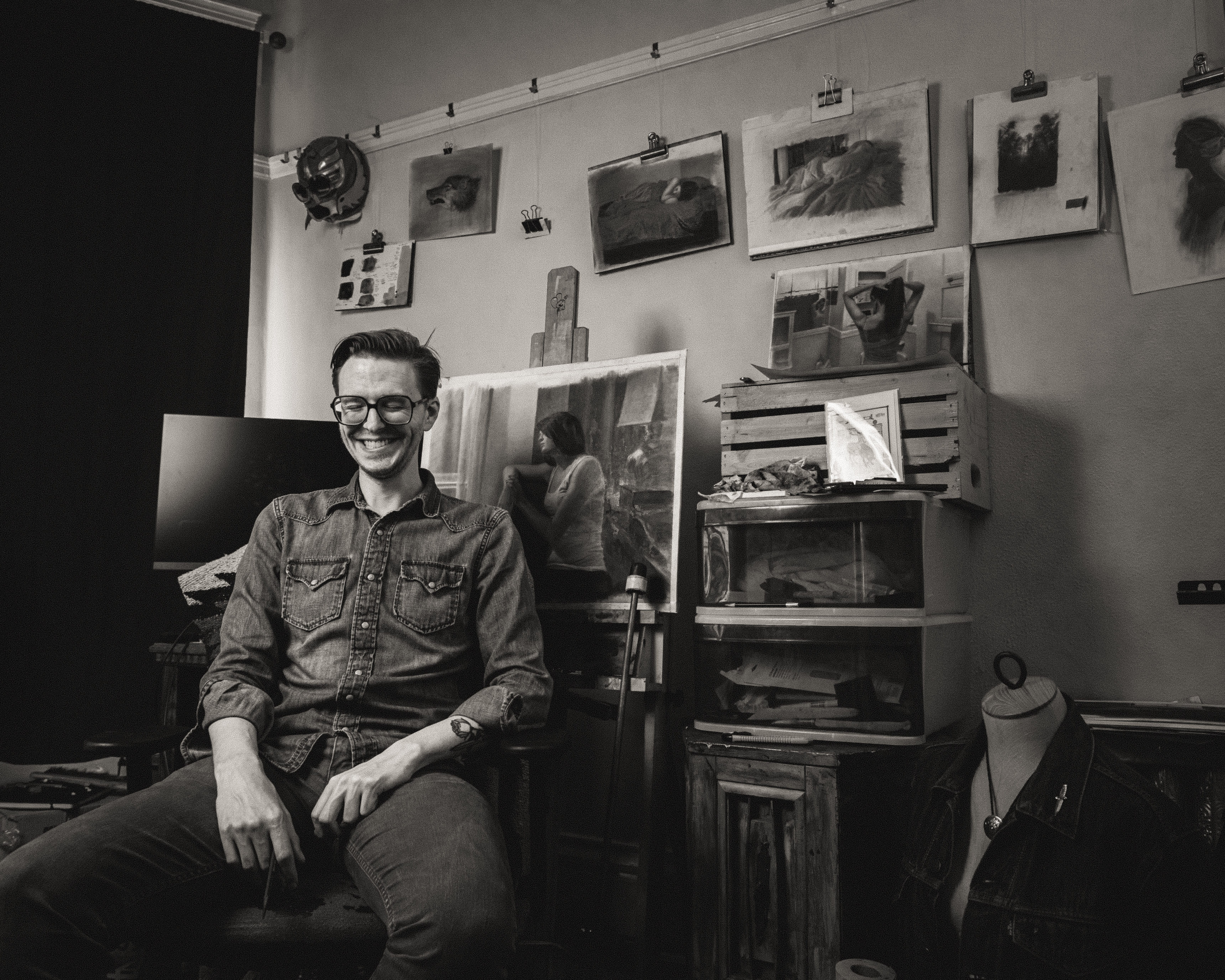 Photo of Zachary Oldenkamp smiling in his studio in front of his drawings