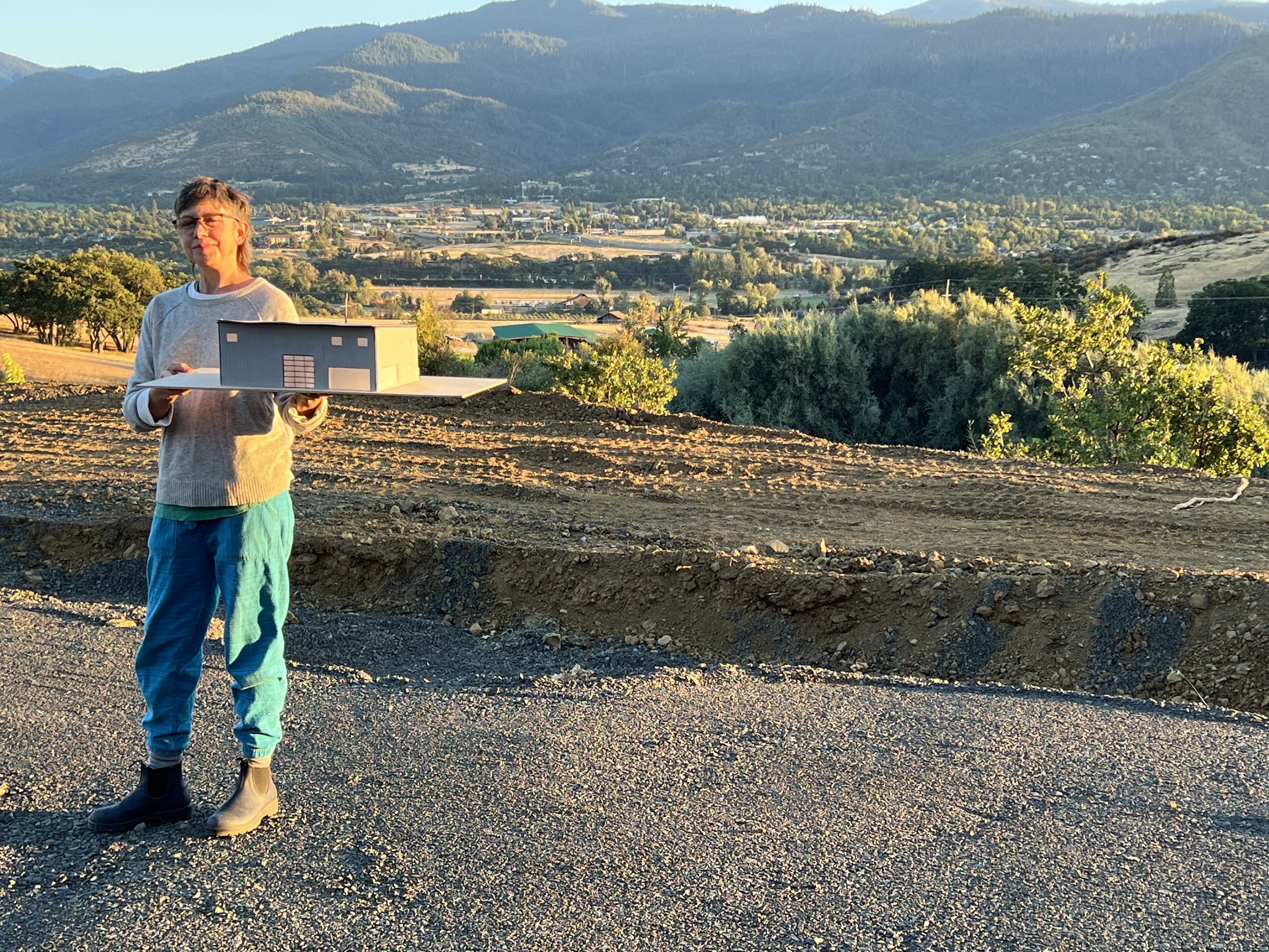 Kristy holds scale model of the building on prepared site. August 2024
