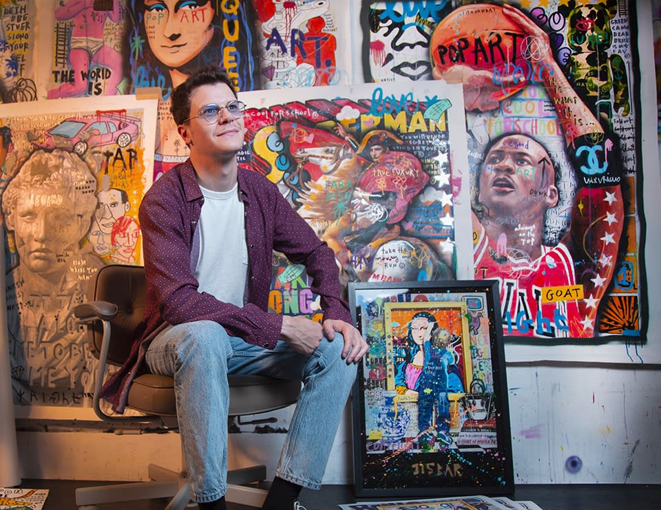 French street artist Jisbar sitting in front of his paintings.