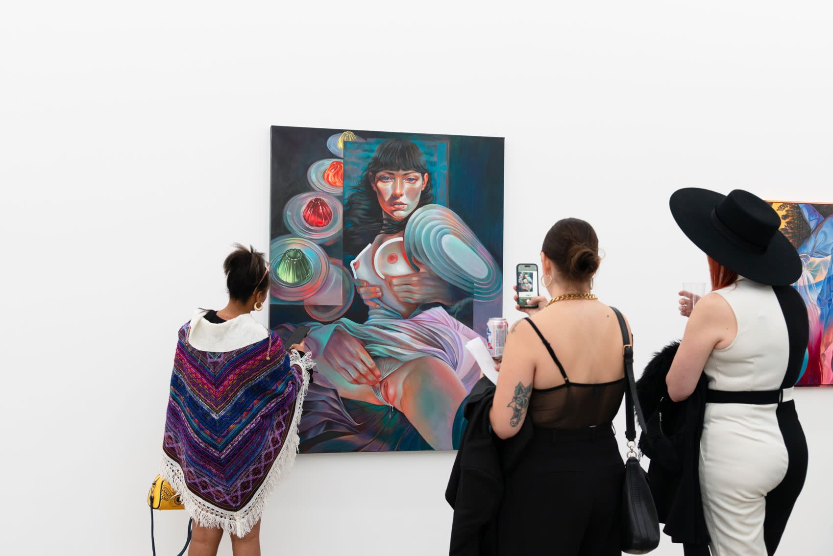 Women stand in front of and take pictures of a colorful painting of a woman, facing the viewers while turning, the hands of a man coming in from out of the frame to caress her.