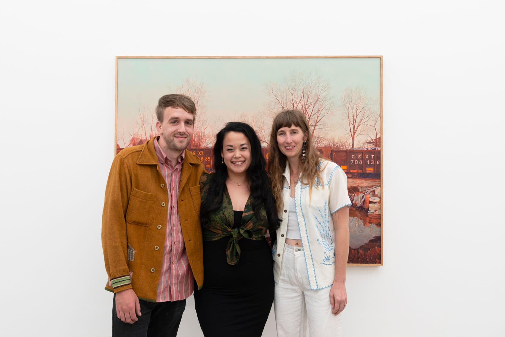 Artist pat Perry poses with LA Director Dasha Matsuura and artist Rosemary Brown in front of one of Perry's painting inside a large whitecube gallery with white walls. Everyone is smiling. 