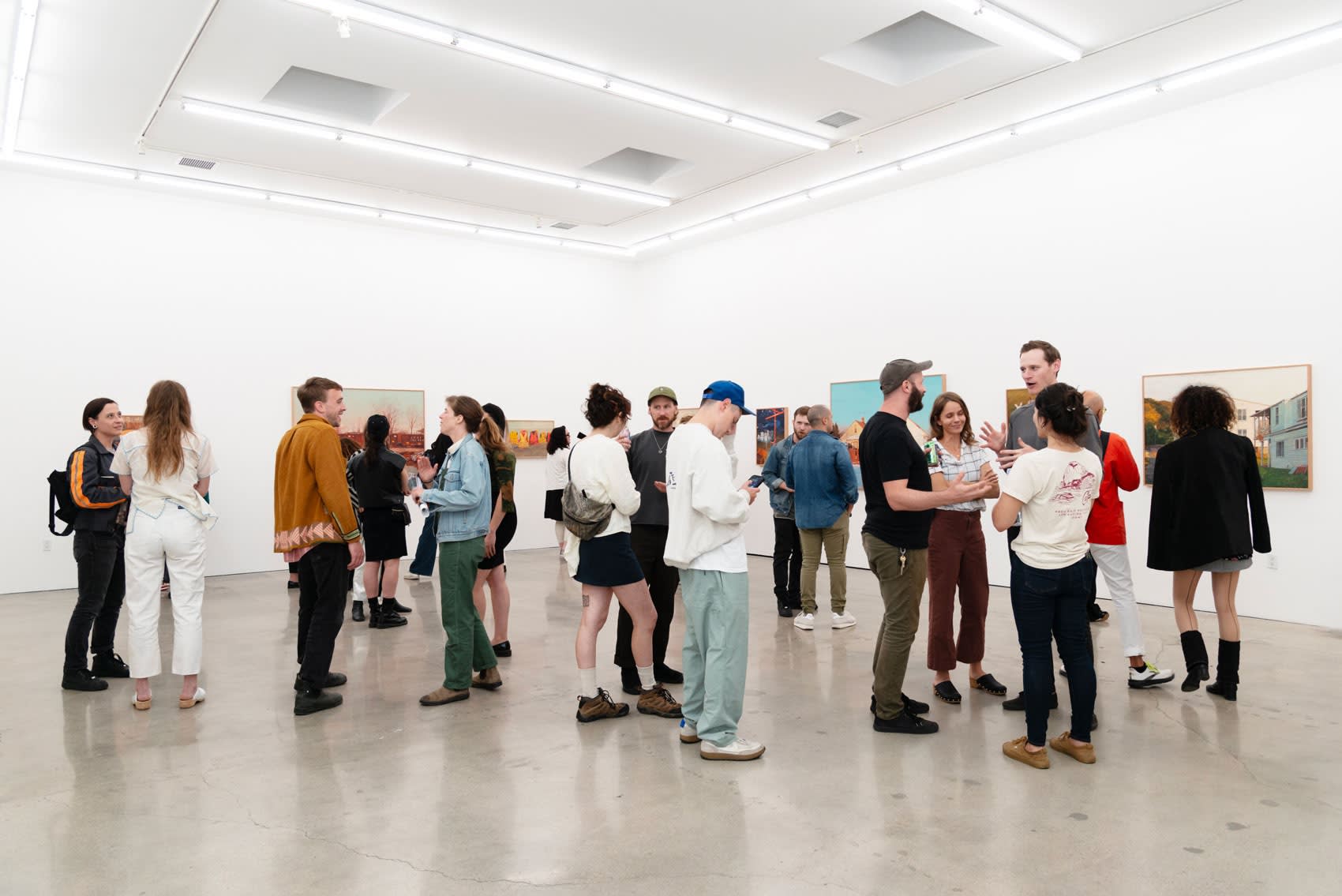 A large crowd of people stand in an art gallery with white walls and a concrete floor at the opening of Pat Perry's solo show which world. 