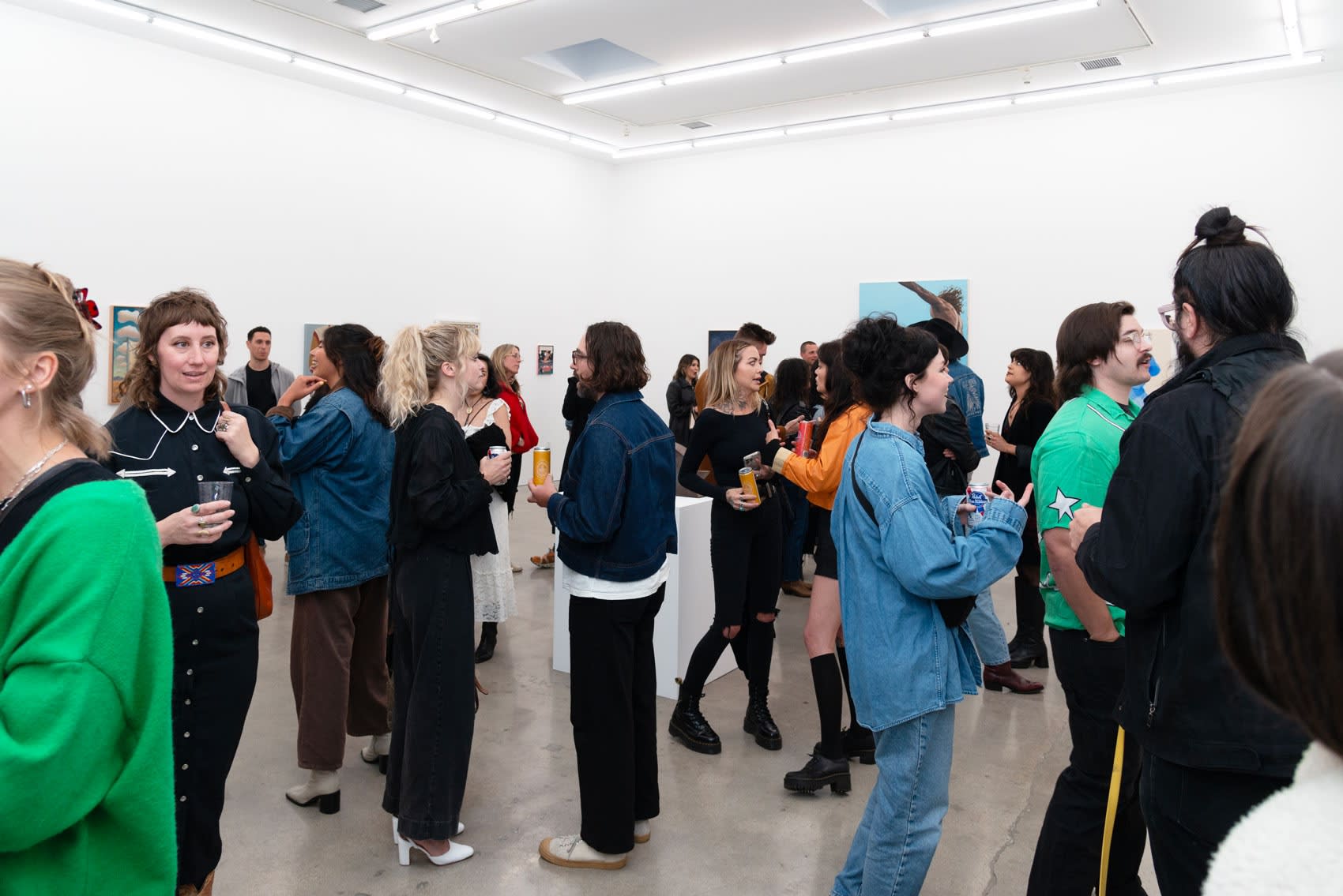 A large group of people standing in the gallery looking at art and talking