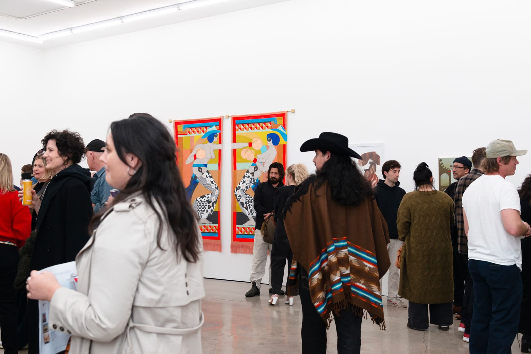 Photo of people standing in the gallery talking and looking at the art on the walls