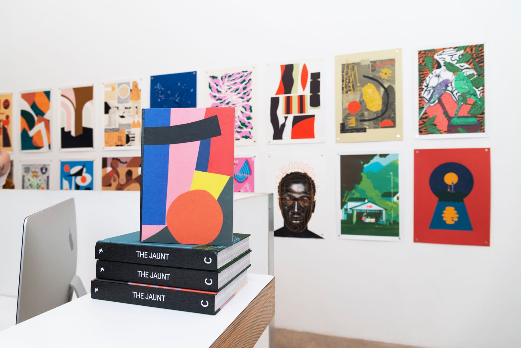 The gallery wall with two rows of print posters and a stack on books on a desk counter