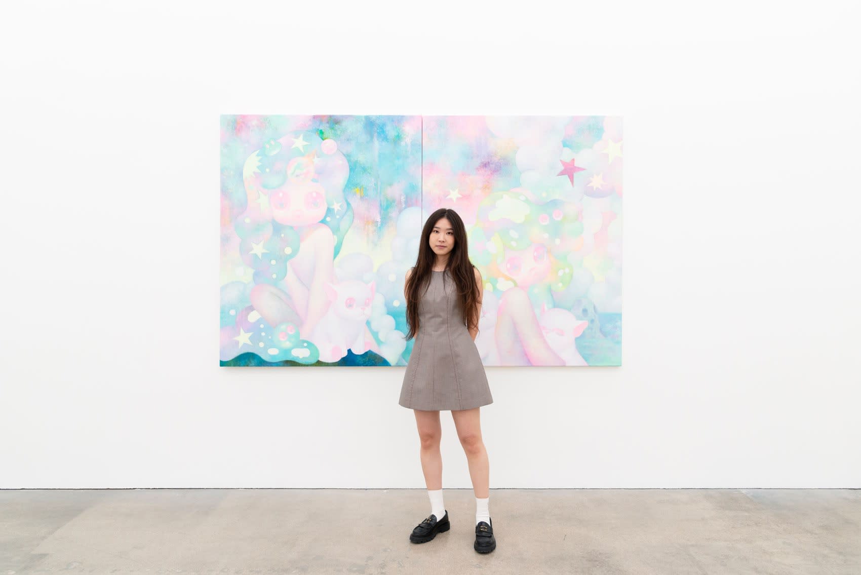 So Youn Lee stands in front of her pastel colored painting in a white wall gallery