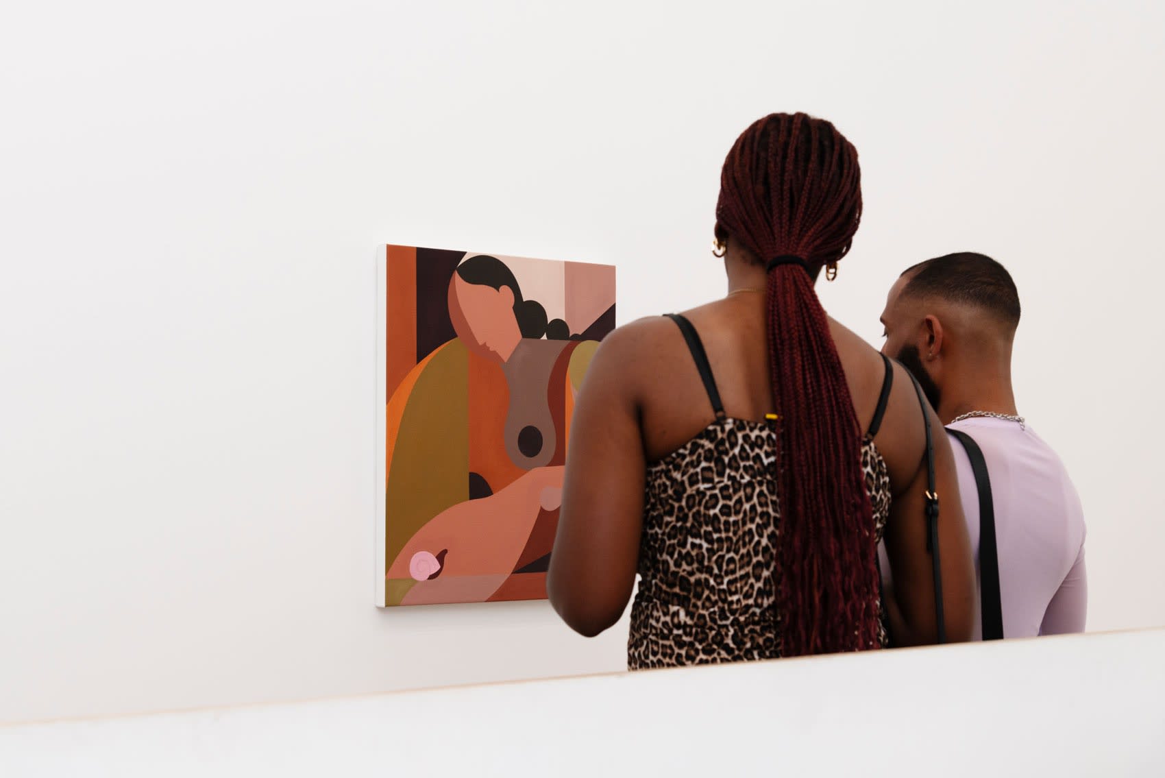 Two people look at Liz Flores's brown and pink neutral colored painting on a white wall.