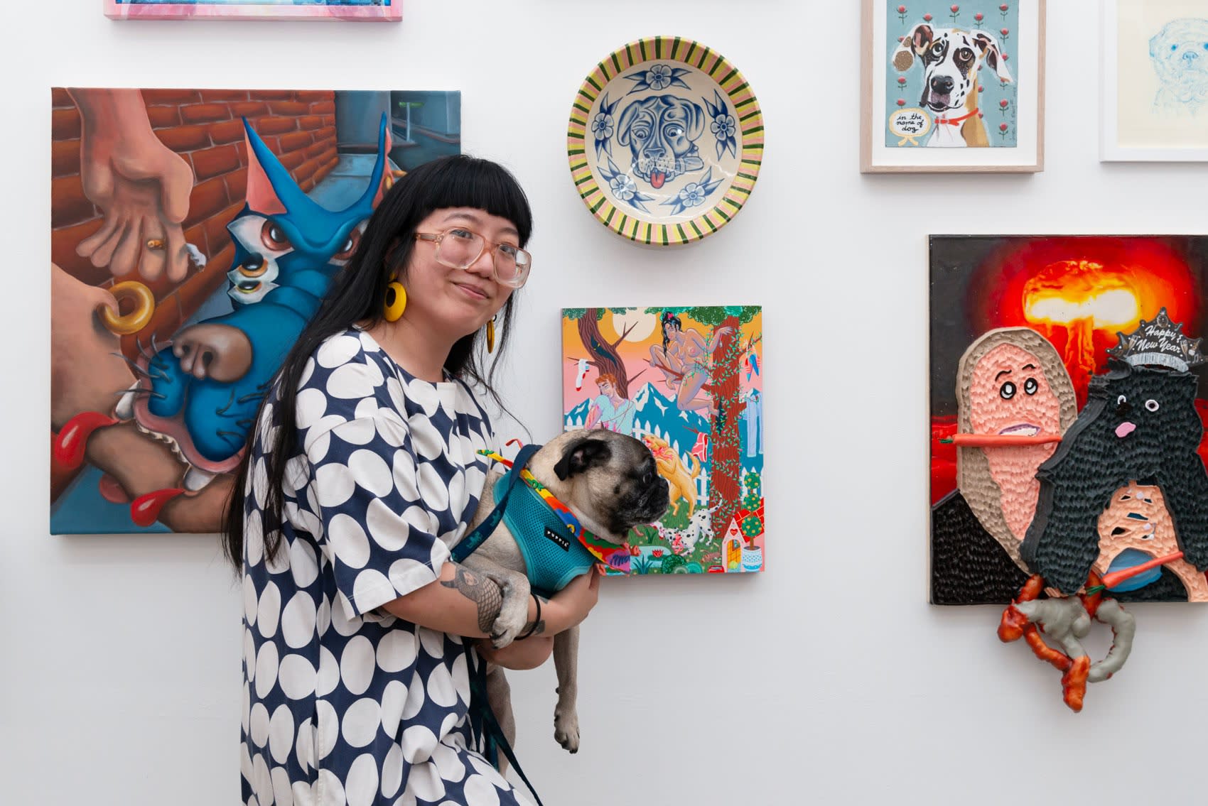 Artist Kristen Liu Wong with her pug in front of a wall of artworks