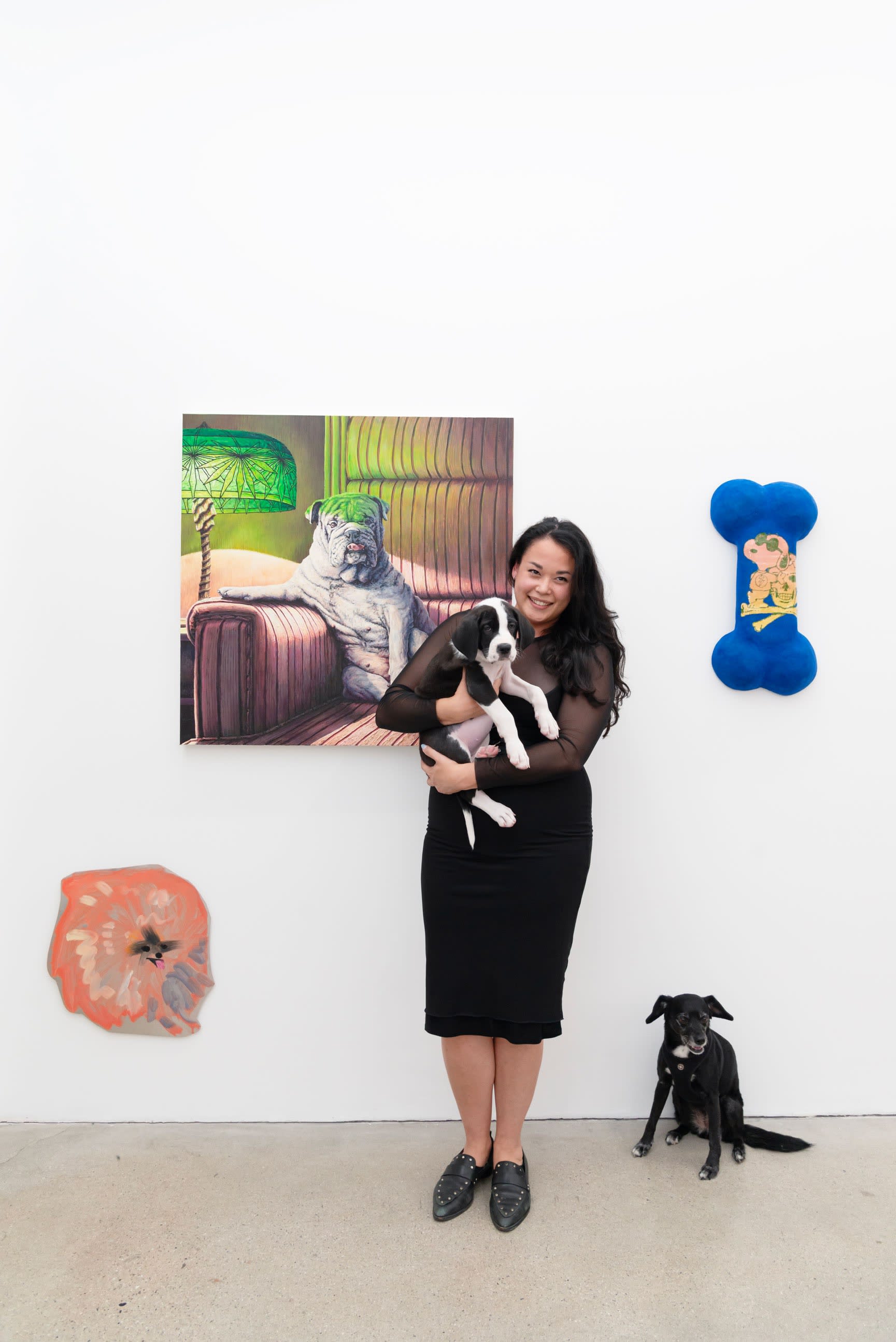 LA Director Dasha Matsuura holding a puppy in front of an artwork while Meera, her black dog, stands next to her