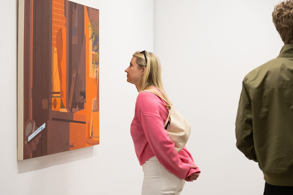 photograph of a woman wearing a pink sweatshirt looking closely at the painting