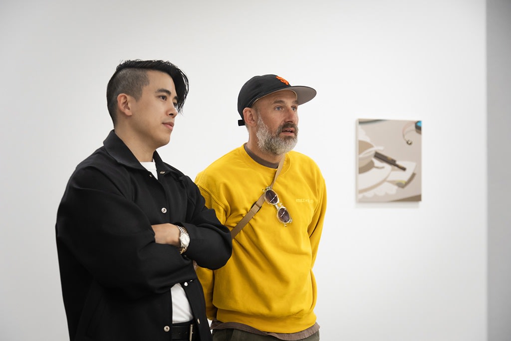 photograph of artist Adrian Kay Wong and a friend looking intently at a painting during the opening reception of his latest exhibition