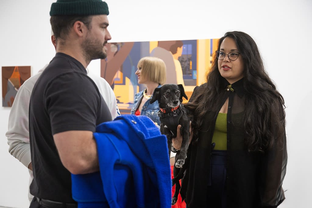 Image of a woman holding a dog as she talks to a man at the opening reception of Adrian Kay Wong's exhibition