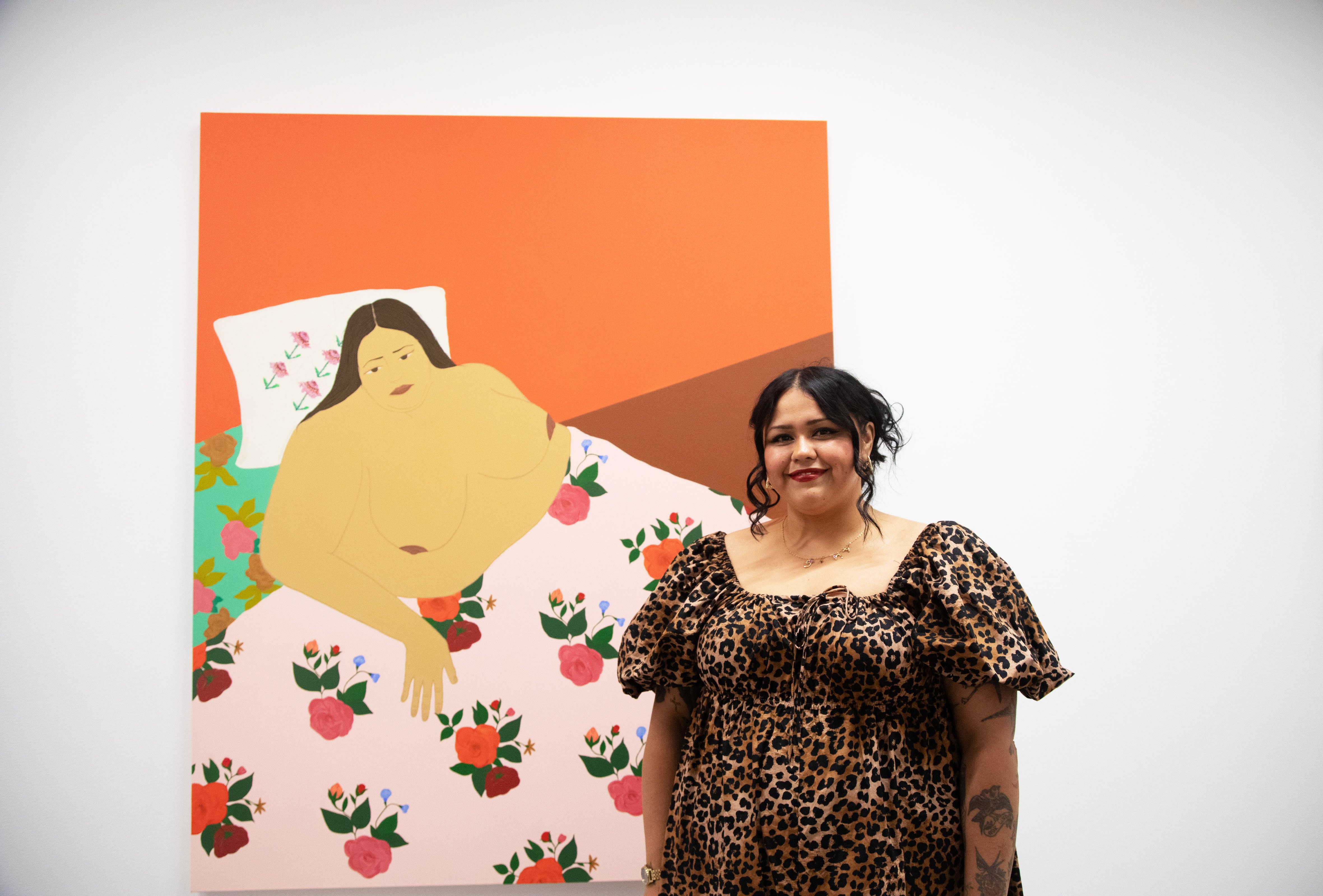 Gina M. Contreras with her large painting Vulnerable Surfaces hanging on a white gallery wall. 