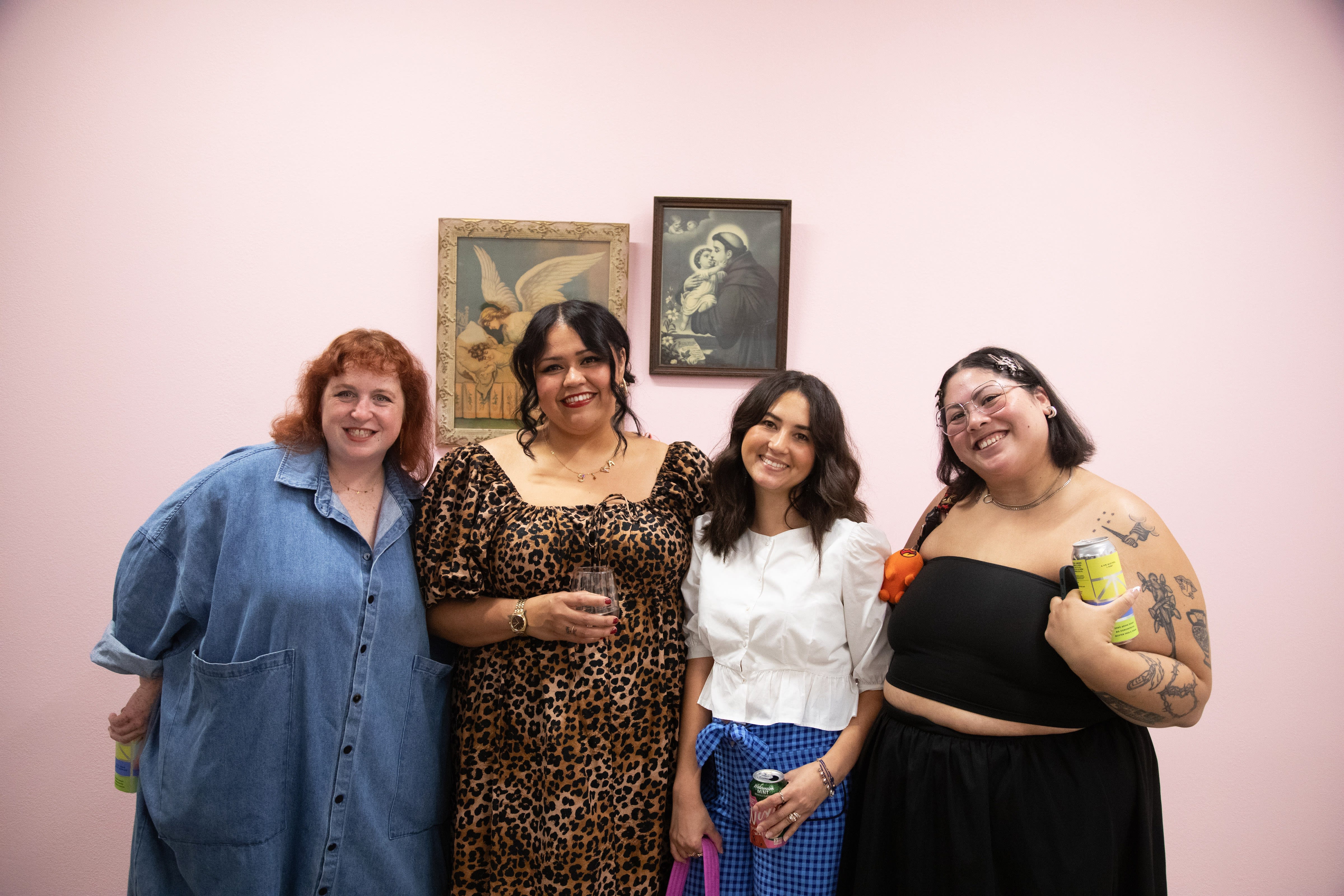 Artist Gina M. Contreras poses with friends in front of her installation on a pink wall in the art gallery. 