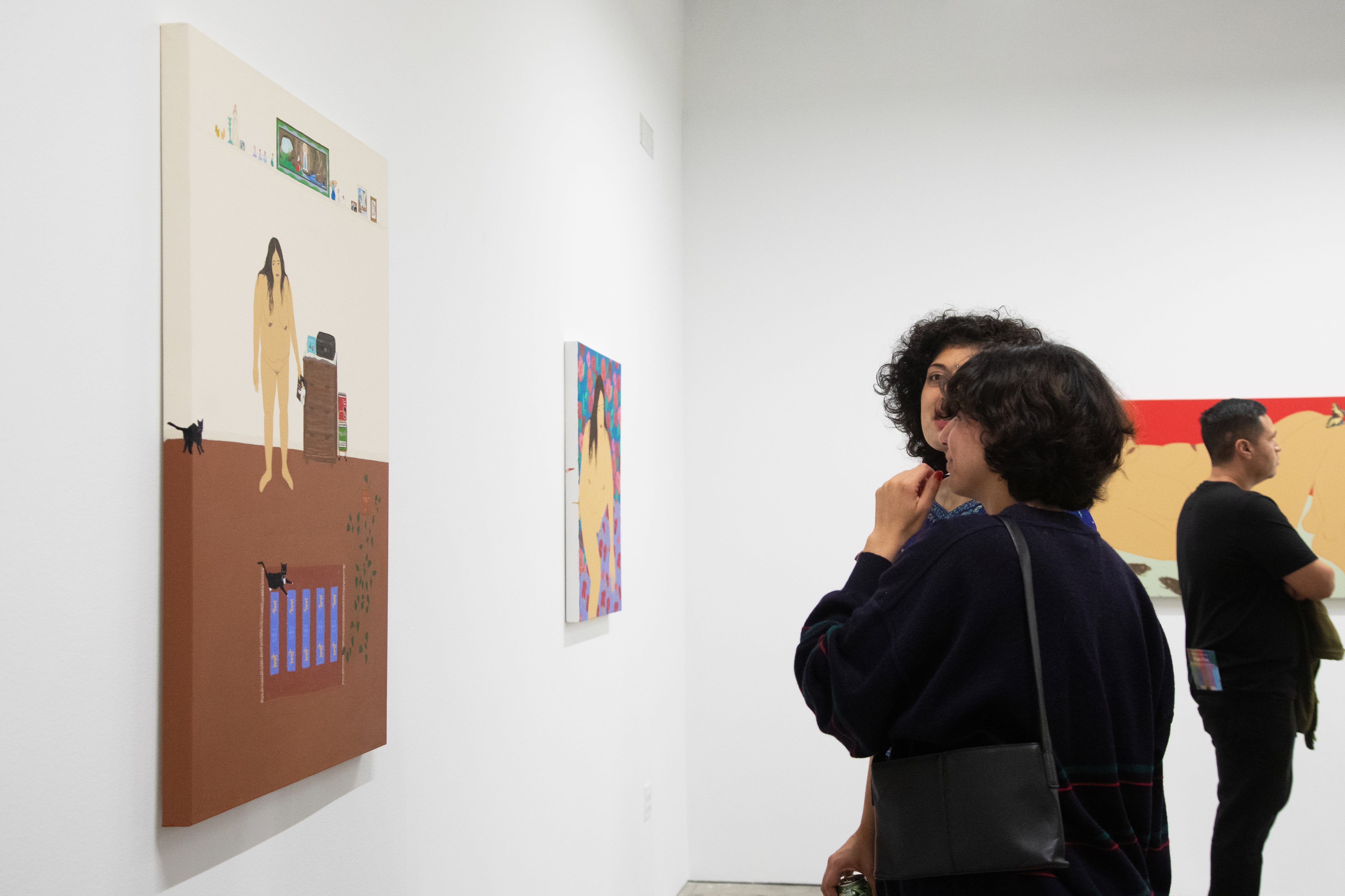 Guests look at paintings at the opening of Gina M. Contreras's solo exhibition Amor Secreto inside a white wall art gallery. 