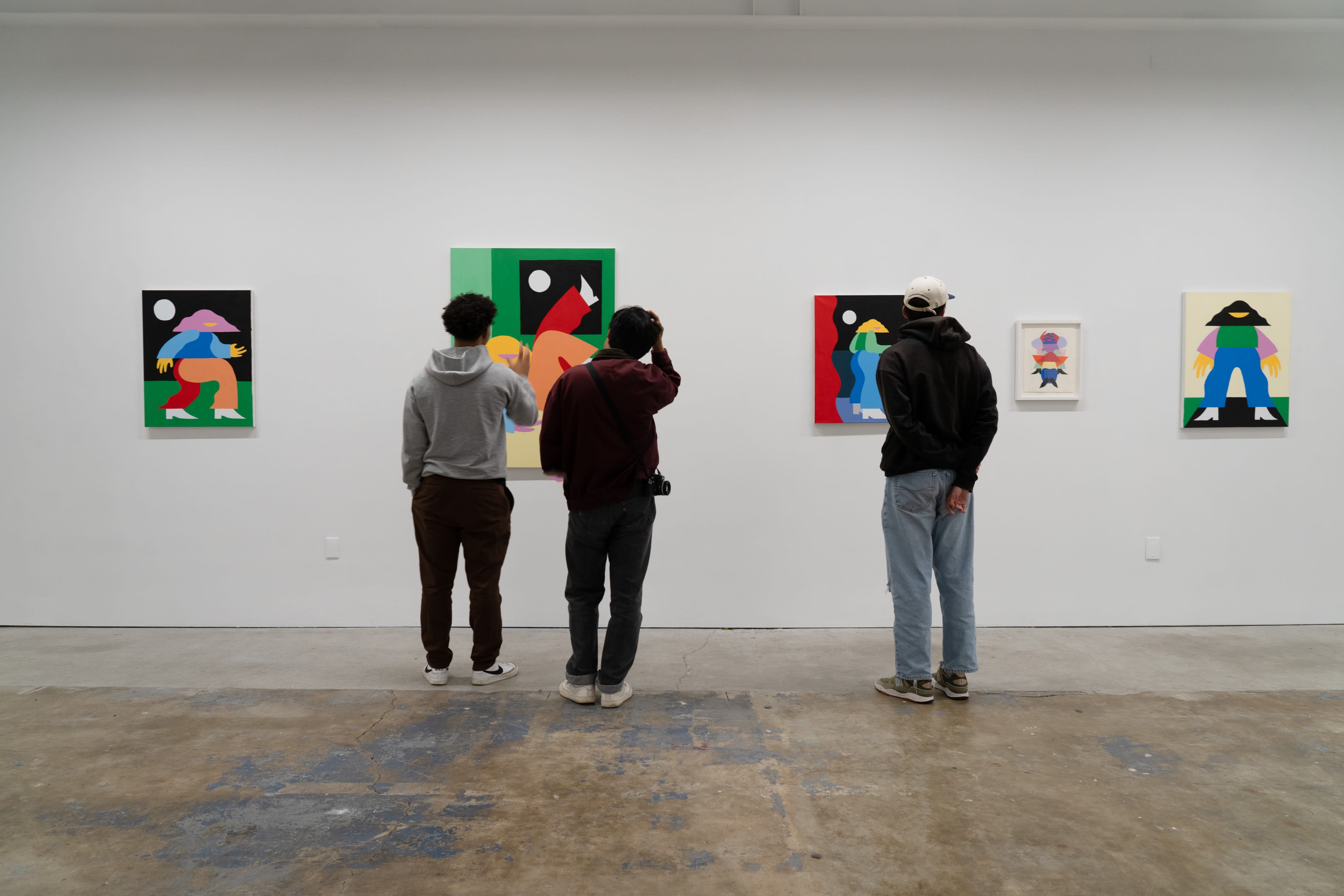 Three men stand in front of paintings at Marbie's show. 
