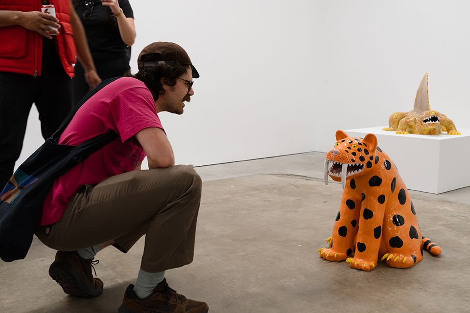 A man in a pink shirt crouches down to admire an orange and black spotted saber tooth tiger, the ceramic 