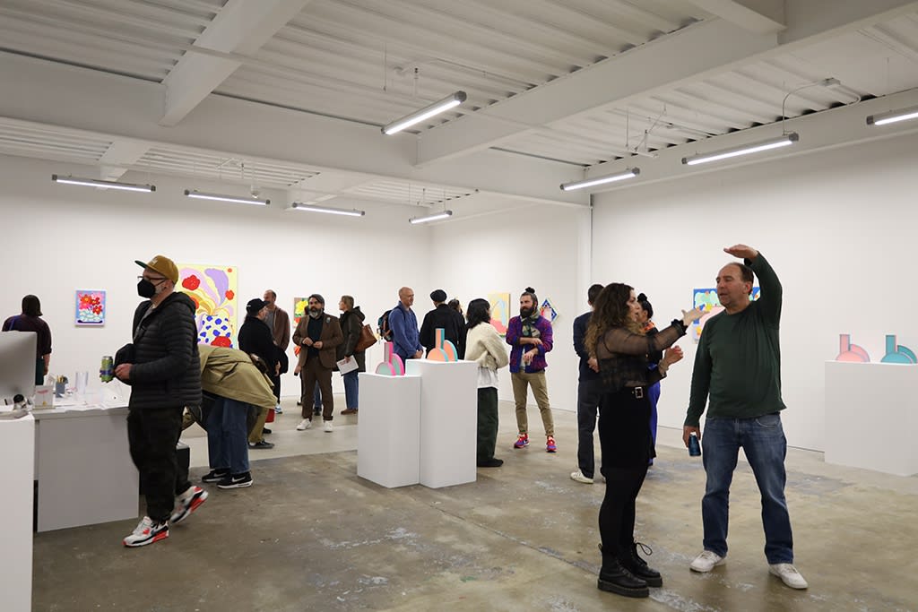 Attendees stand inside a white wall gallery among sculptures, paintings, and multimedia artwork on the wall at the opening of Cosmic Bloom, an art exhibition featuring CHIAOZZA and Rachel Strum. 