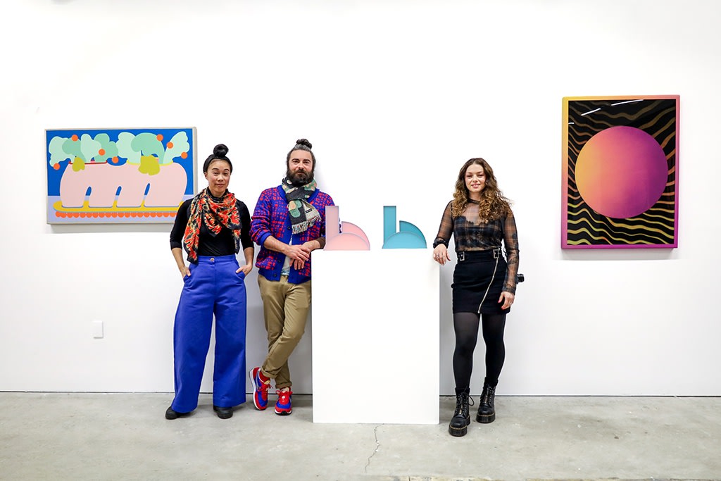 Terri Chiao, Adam Frezza, and rachel Strum stand with their artworks in a white wall gallery for their exhibition 