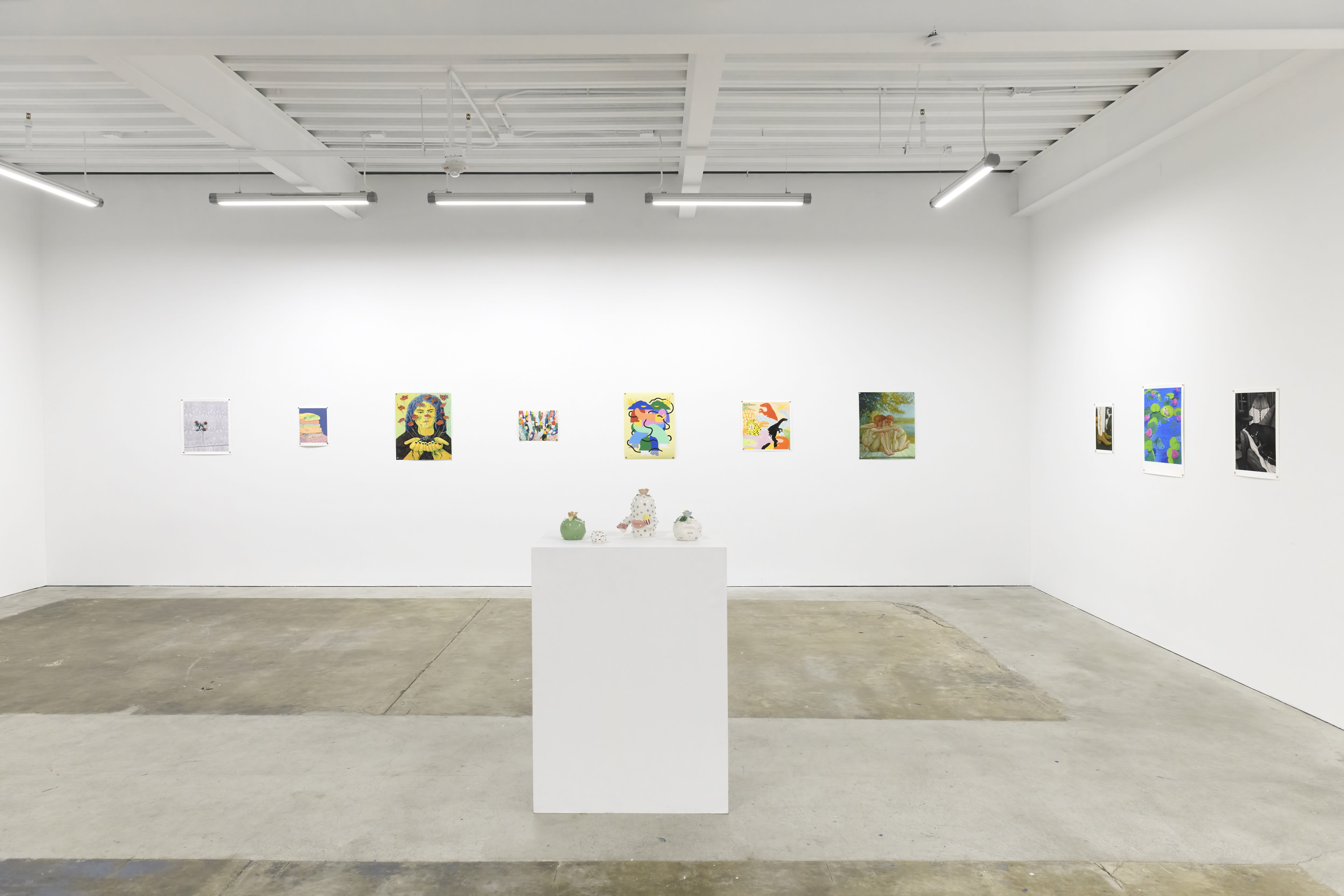 Photo of prints on a white wall in an art gallery and small ceramic sculptures on a pedestal. 
