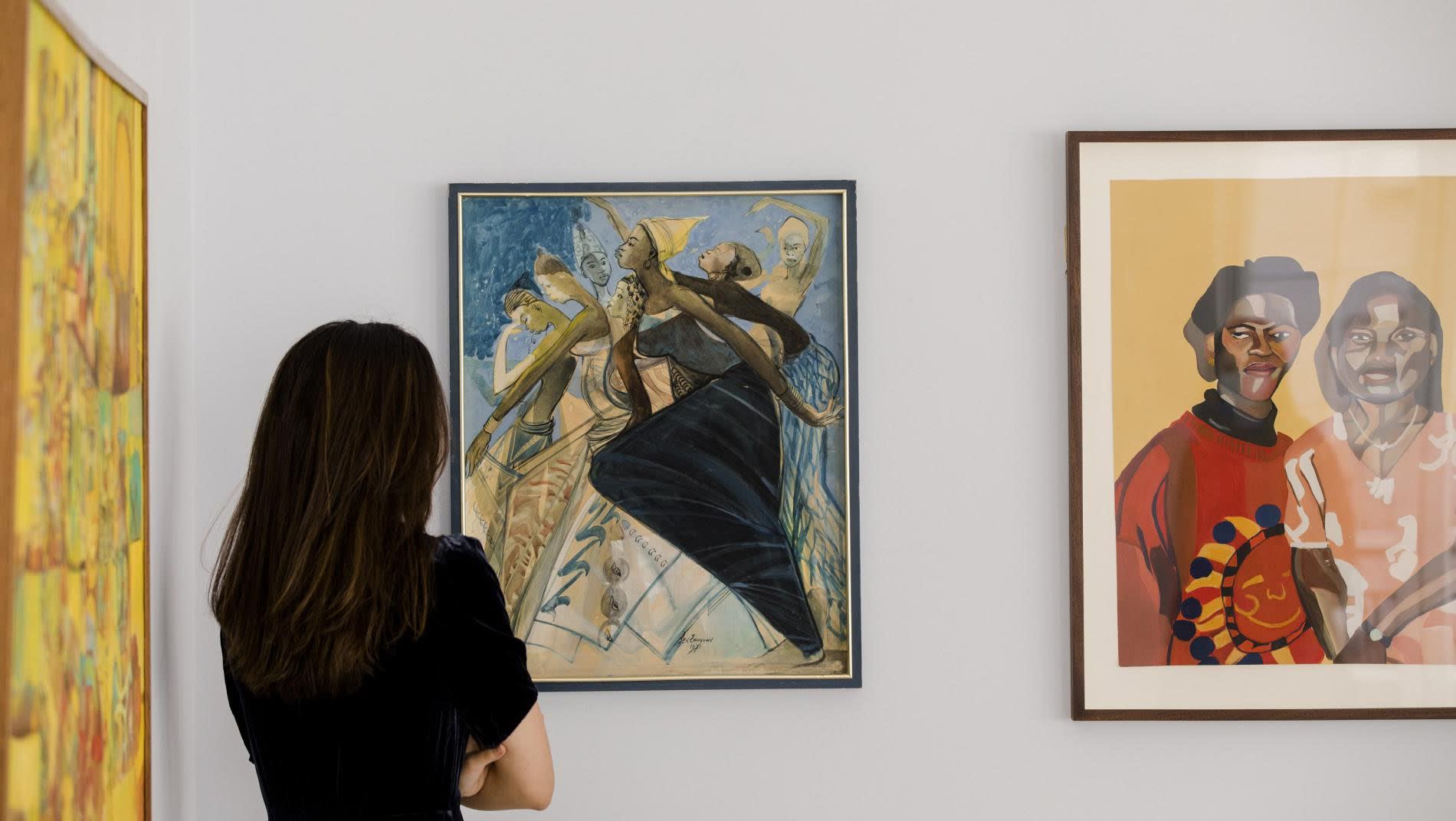 woman looking at two paintings from african Artists at an auction house