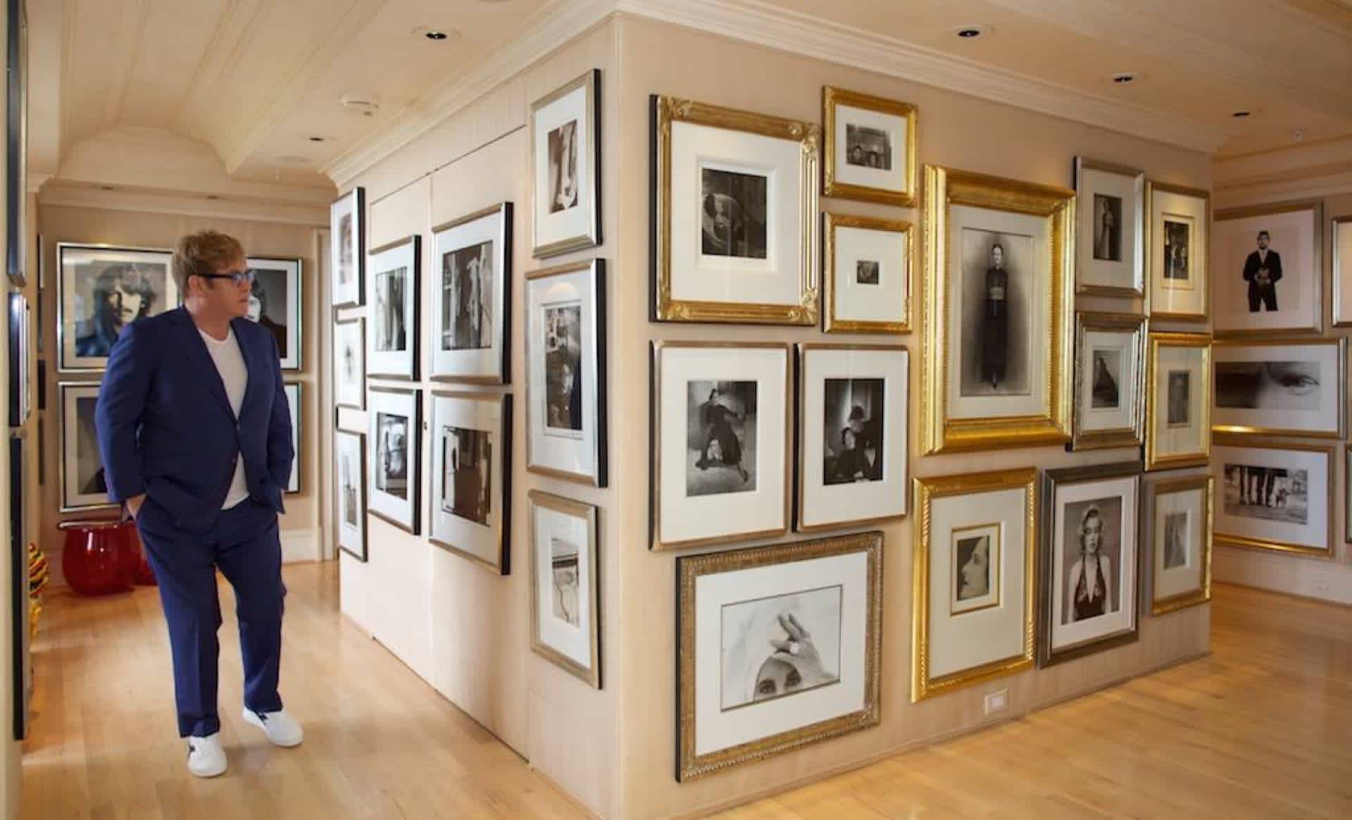 Four walls of the Elton John photography collection with the musician Elton John standing in front of them.