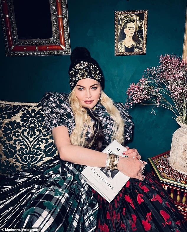 Madonna sitting in front of a picture of Frida Kahlo, which is part of the Madonna art collection.