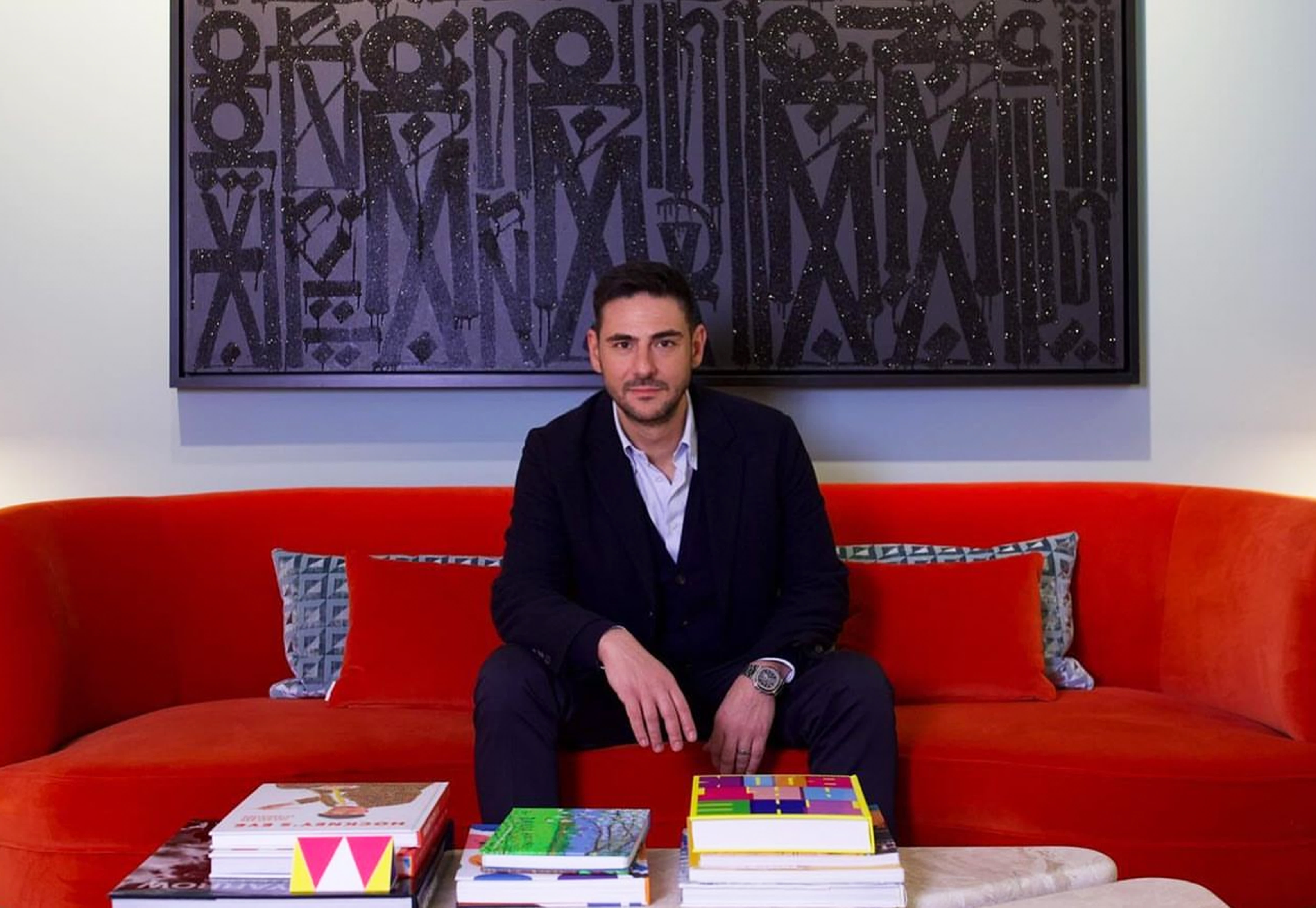 Mario Zonias, expert Maddox art advisor sits on a red couch in front of a RETNA print, ready to assist clients to consign art from their collections.