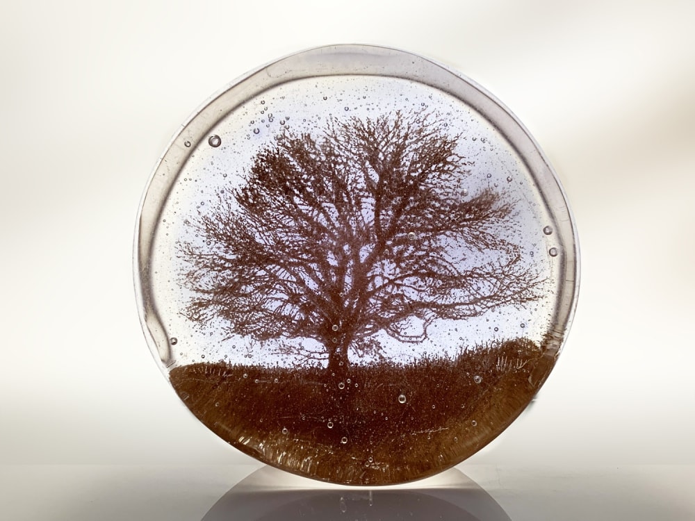 Helen Slater round glass art piece with a silhouette of a tree in sepia against a pale lilac background.