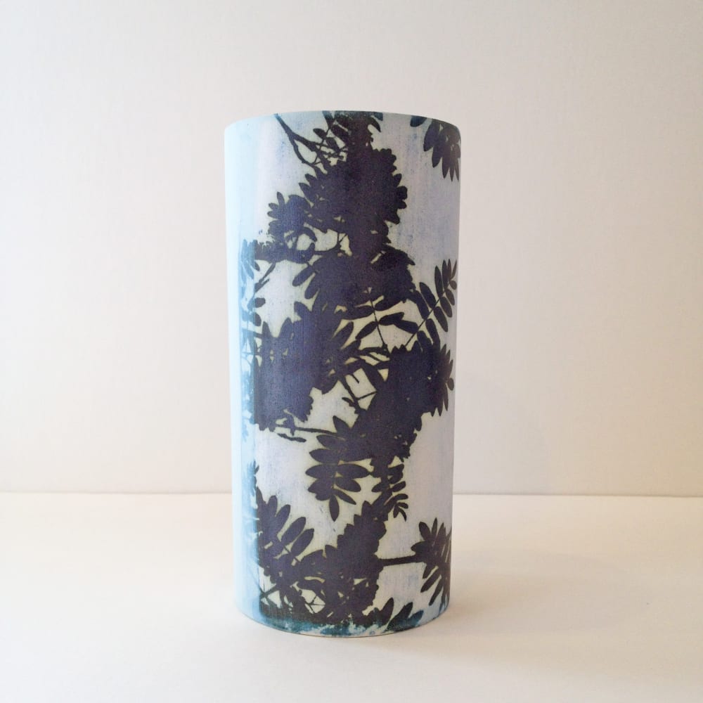 A ceramic vase by Kit Anderson in duck egg blue with overhanging branches of leaves.
