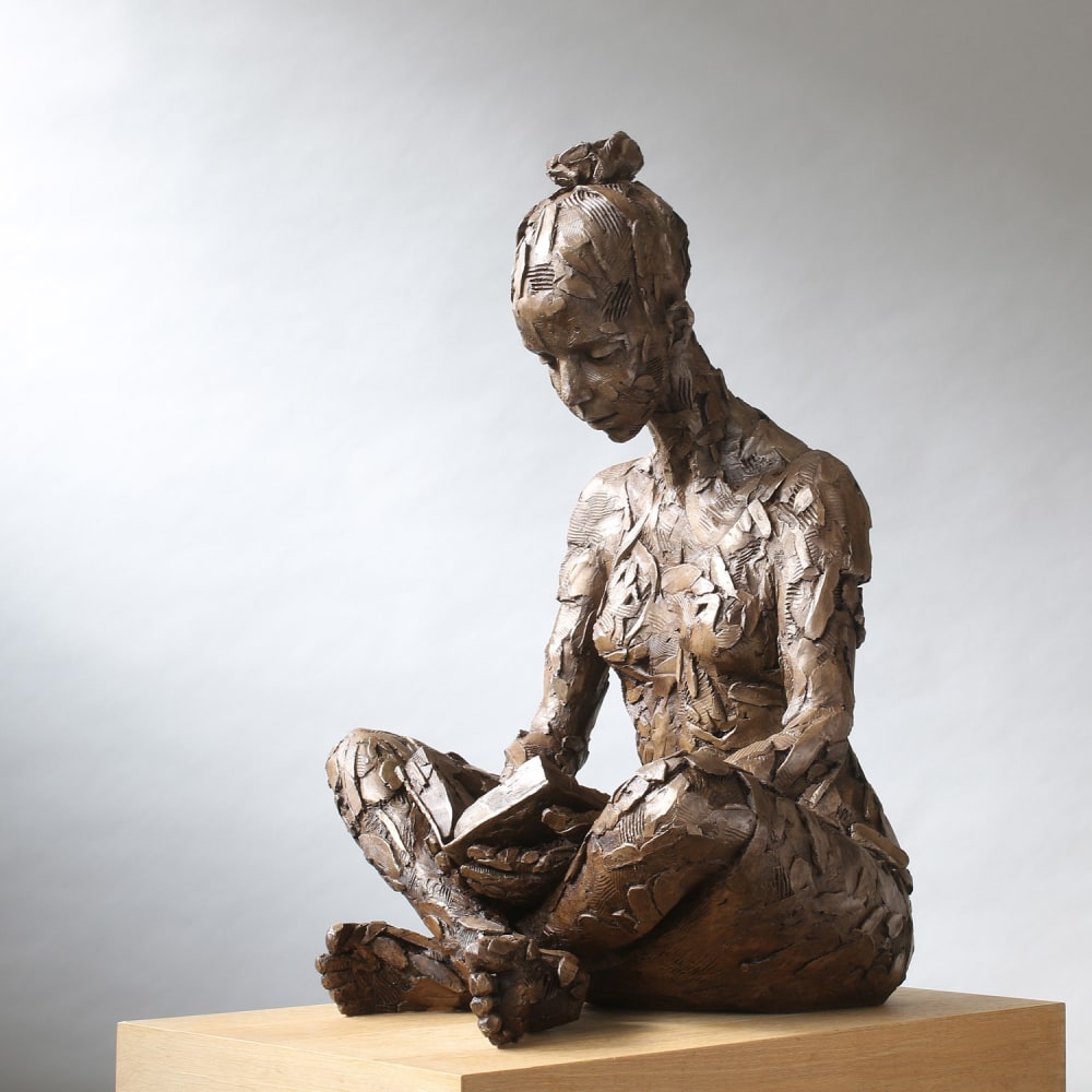 Carol Peace sculpture of a female figure sitting cross legged reading a book resting in her lap.