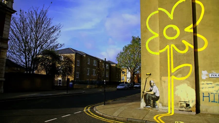 Banksy’s “Yellow Lines Flower Painter” mural featuring a road worker slumped beside a daisy growing from double yellow lines, originally painted in East London, 2007.