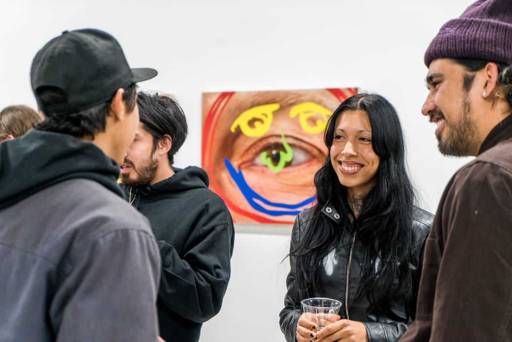 photograph of 4 people standing in a gallery and smiling - artwork on the wall behind them