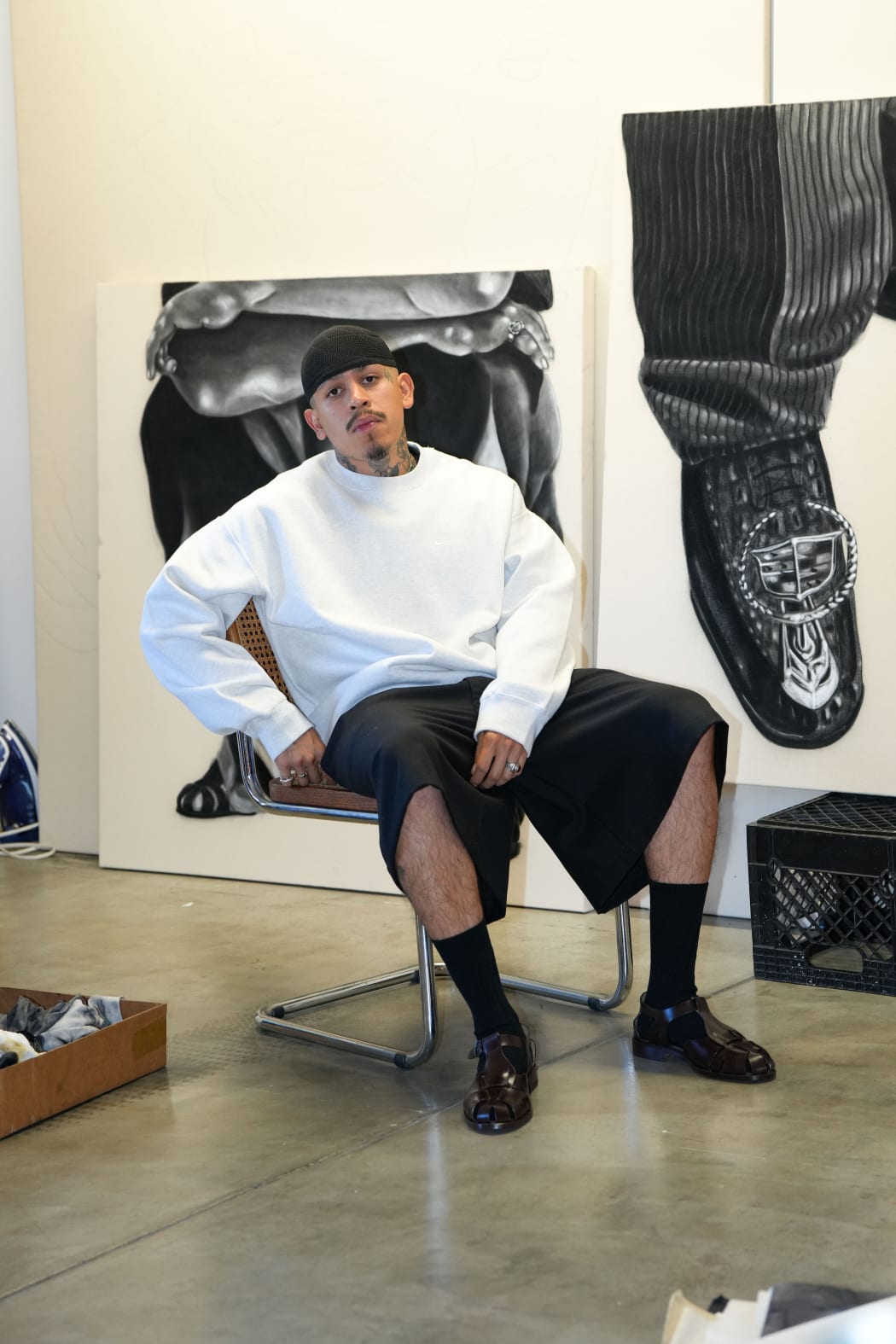 photo of the artist Esteban Samyoa sitting in a chair in his studio with paintings behind him