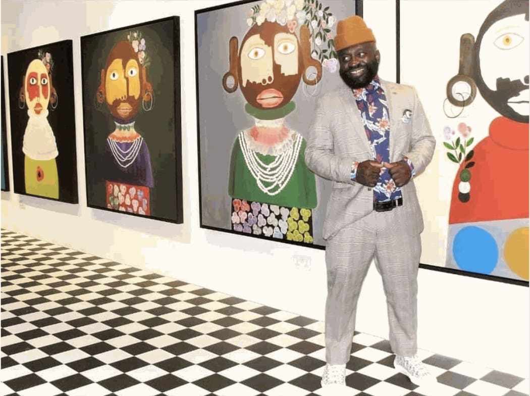Artist Kojo Marfo standing in the gallery room of his solo exhibition, with four of his works in the background