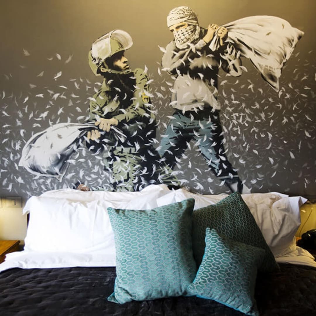 A painting by Banksy of an Israeli border police officer and a Palestinian man having a pillow fight above the bed in one of the rooms in the Walled Off Hotel