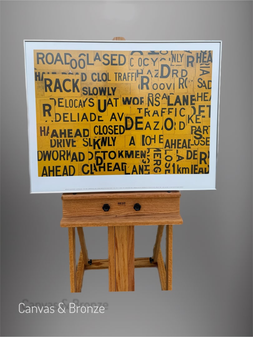 "Road Closed" artwork featuring a collage of yellow and black text elements on a wooden easel, emphasizing urban themes and transportation signs.