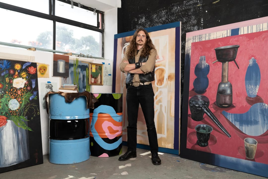 photo of the artist in his studio with a paintings behind him