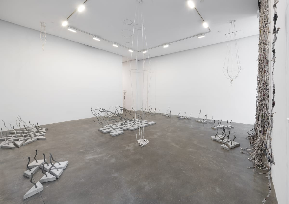 Installation view with many concrete and wire rope sculptures on concrete floor