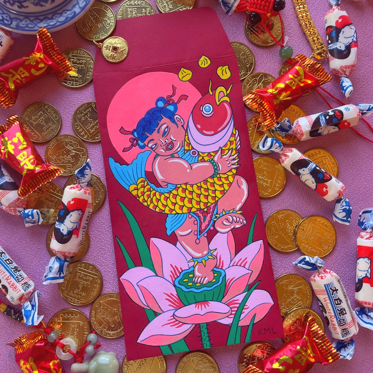 Kristen Liu Wong red envelope with painting of woman and fish. Envelope surrounded by gold coins and candy