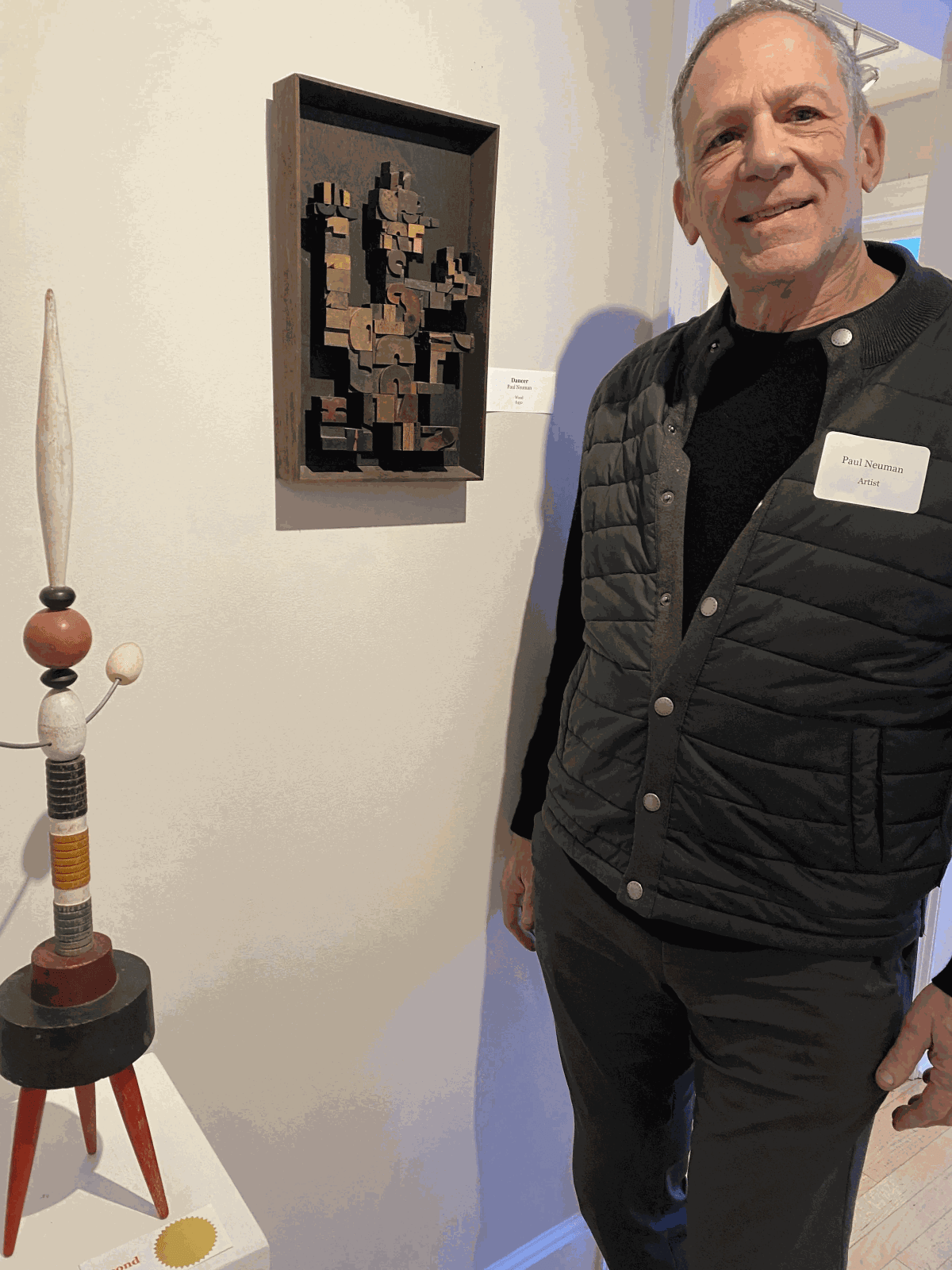 Paul Neuman standing in front of two of his artworks, two sculptures in which one is wall mounted.