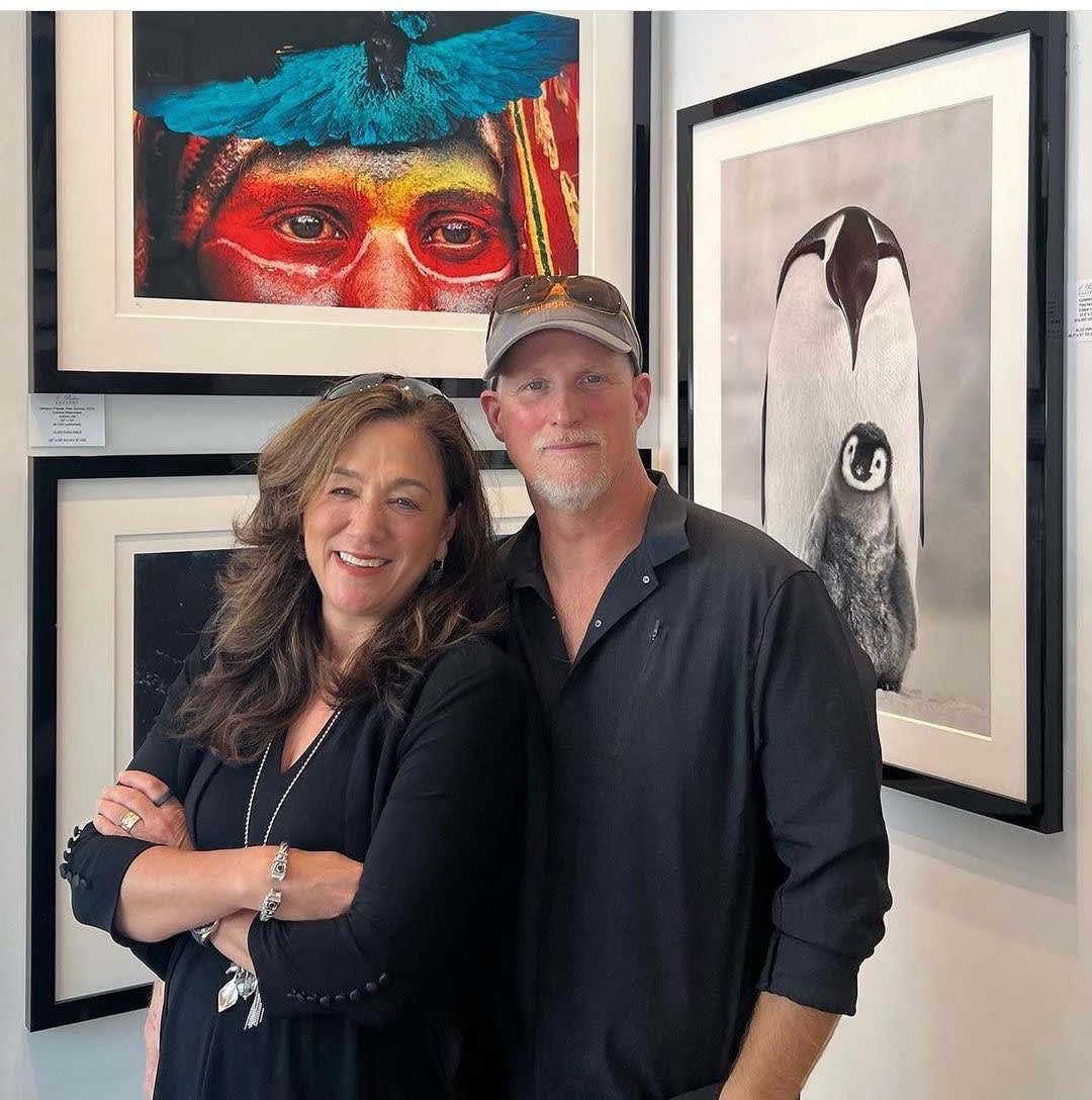 the two artists stand in front of their photographs that are framed on the wall