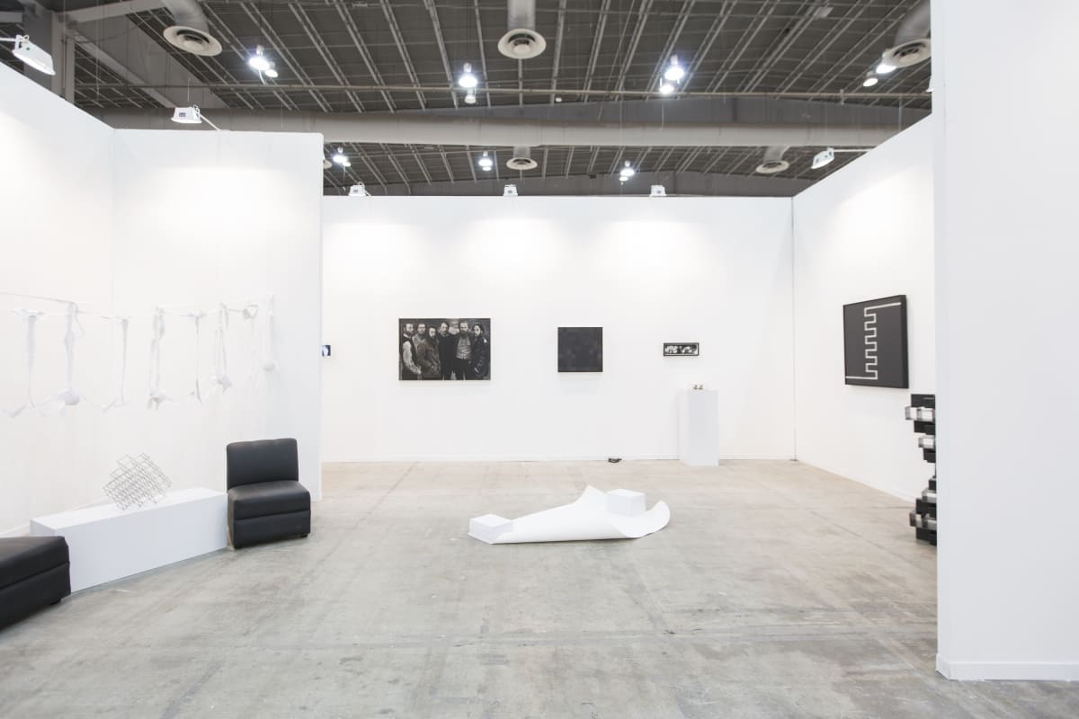 Art fair booth with two abstract steel sculptures, an installation of cut fabric shirts, and three paintings, among other objects. Everything is in shades of black and white.
