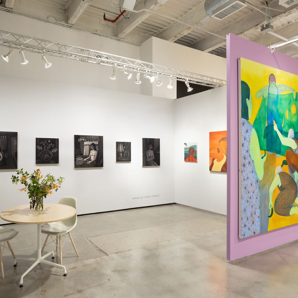 Hashimoto booth at Future Fair; purple wall with large green and yellow painting of women. To the left, table and chairs with flowers on tabletop. Back wall a series of black and white paintings