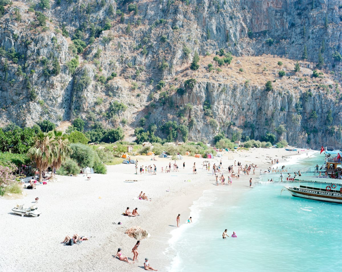 people on beach and swimming in blue ocean with cliffs in background, Butterfly Valley, Turkey, by Massimo Vitali