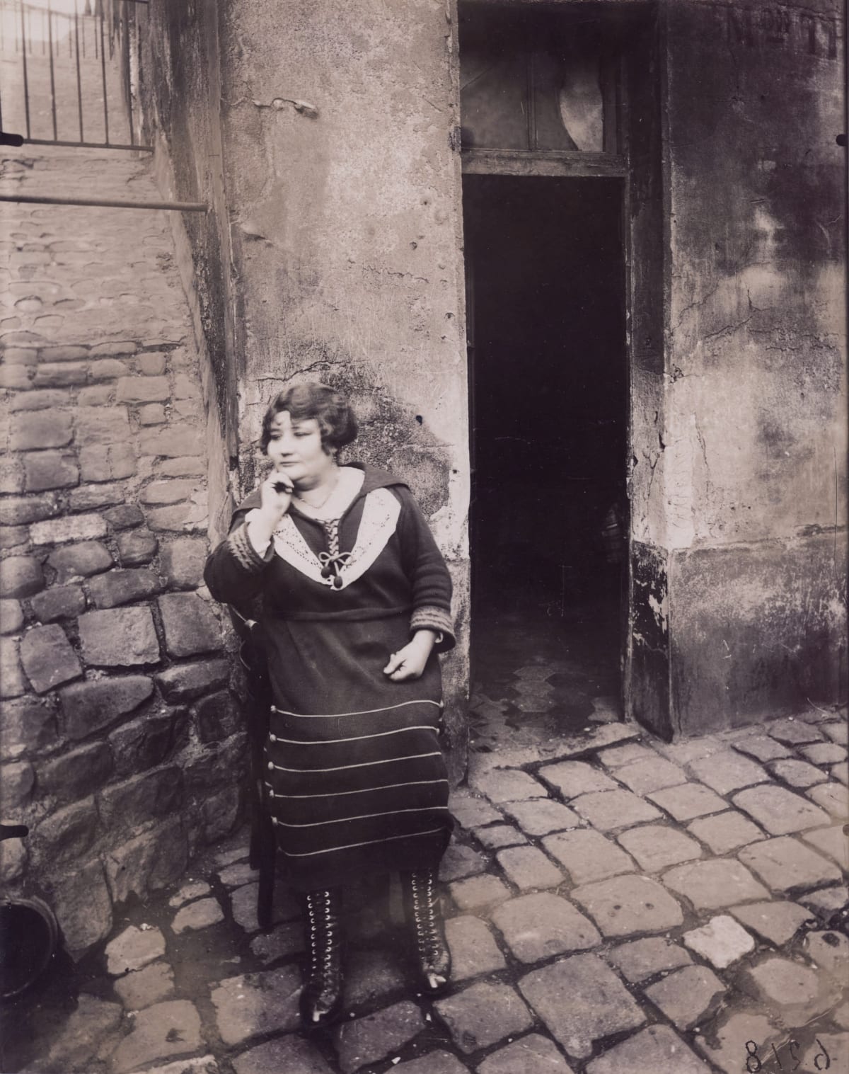 woman standing in street in 1920s Paris with door open behind her
